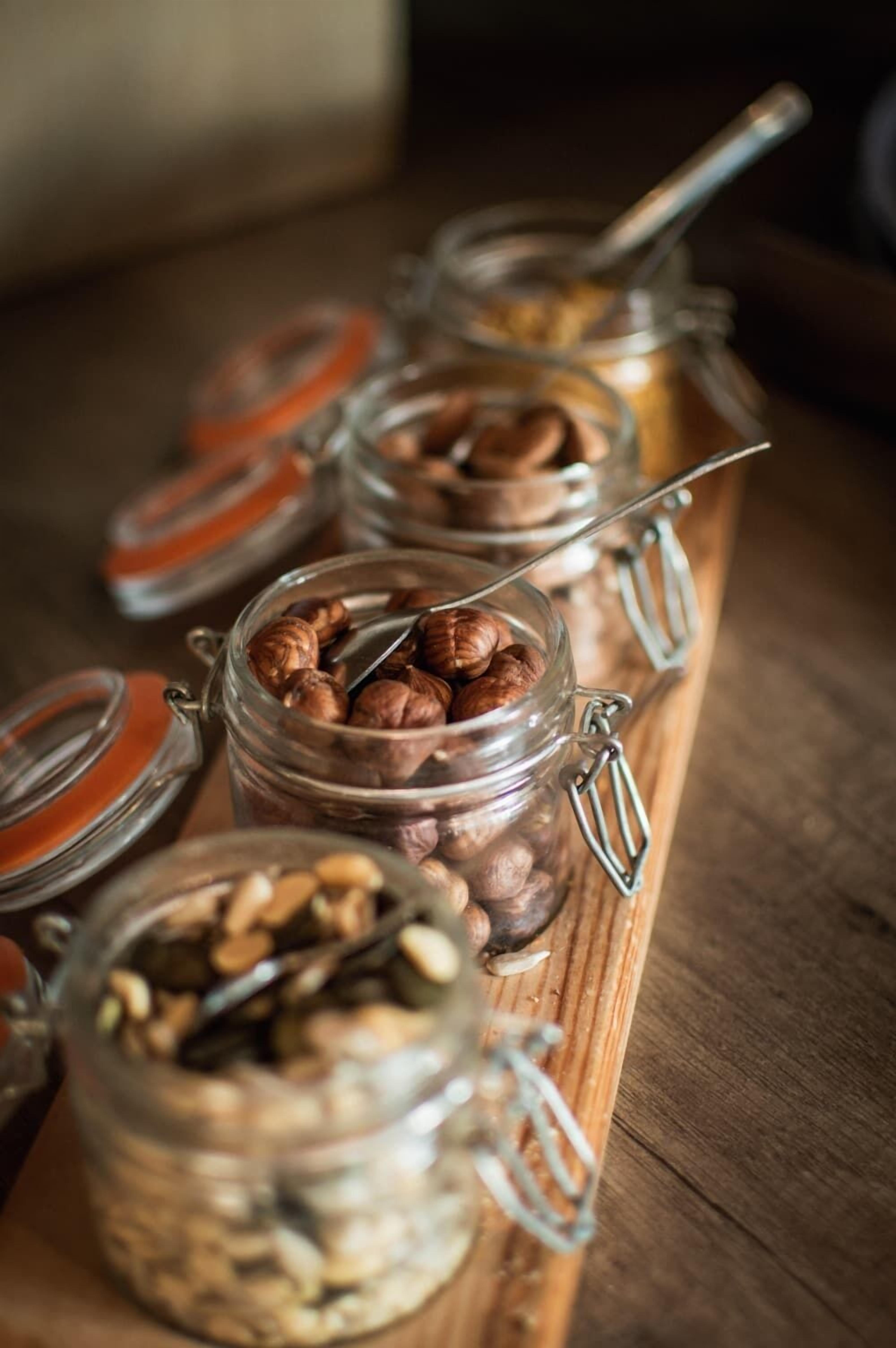 A wooden serving board with glass jars containing various nuts and seeds.