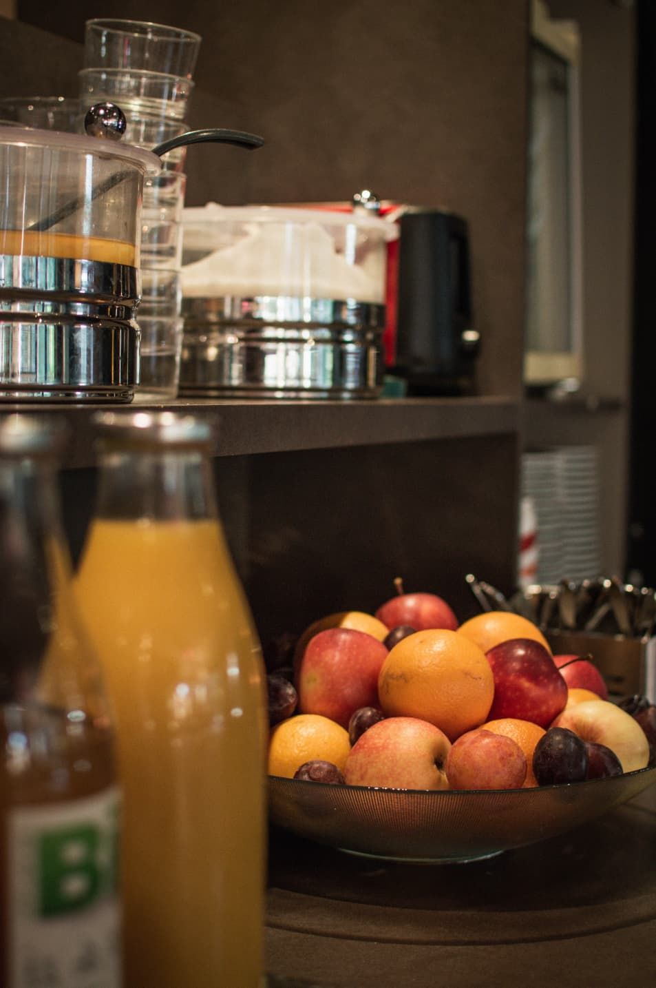A kitchen counter with a fruit bowl, a glass pitcher, and a bottle of juice.