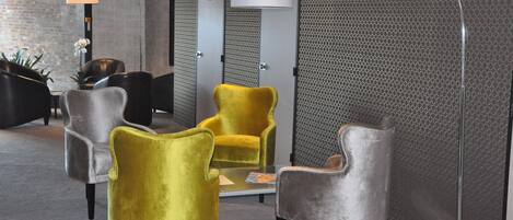 Un lobby moderno con un área de descanso que incluye una mezcla de sillas grises y amarillas, una mesa de centro de vidrio y una pared con un diseño llamativo.