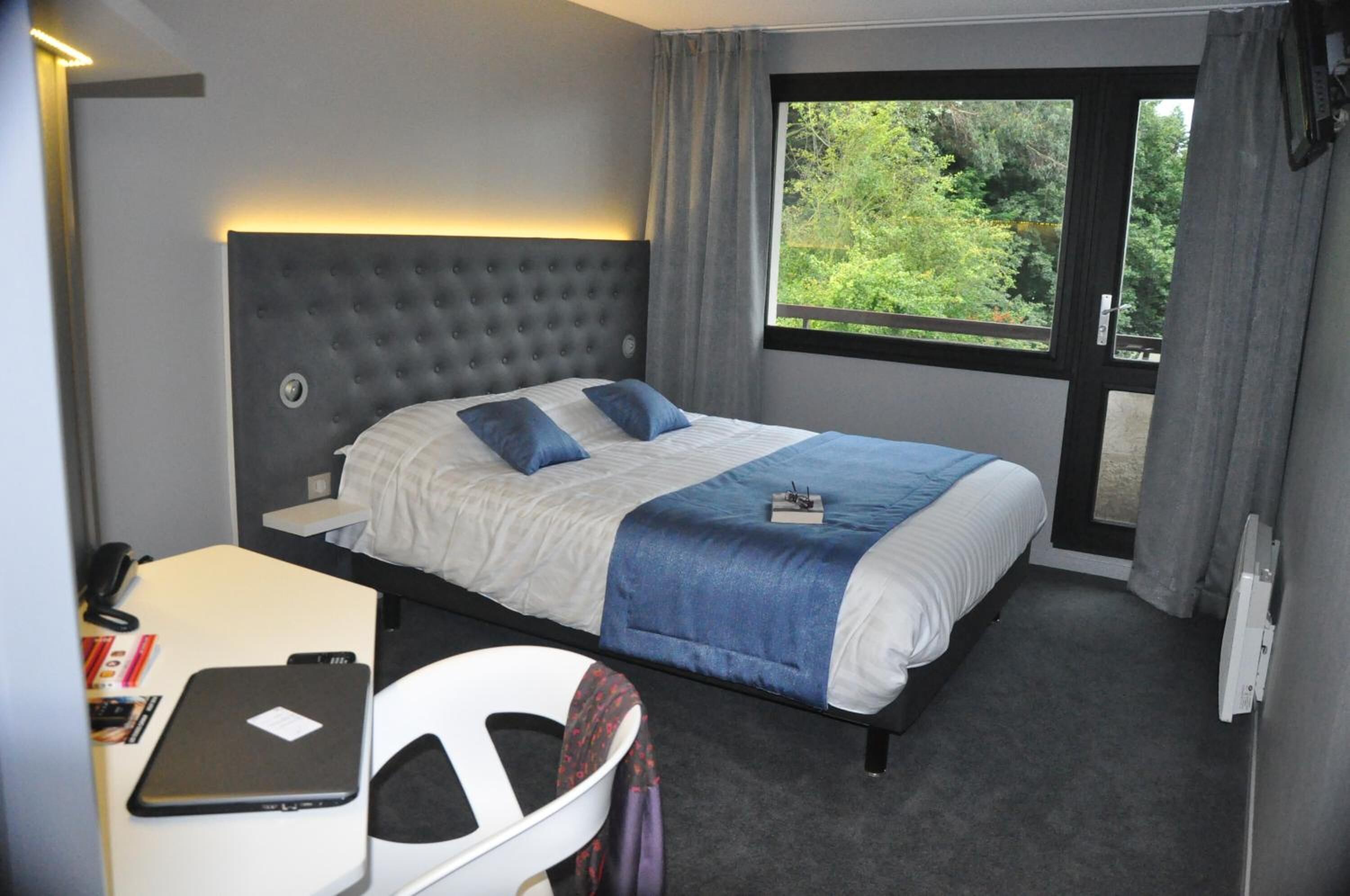 Een hotelkamer met een groot bed, een bureau met een laptop en een raam met uitzicht op groen.