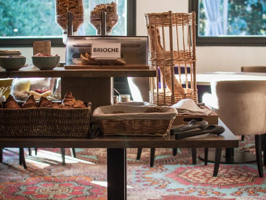 A table with a sign reading 'BRIOCHE' and various food items, a wicker chair, and a patterned rug.