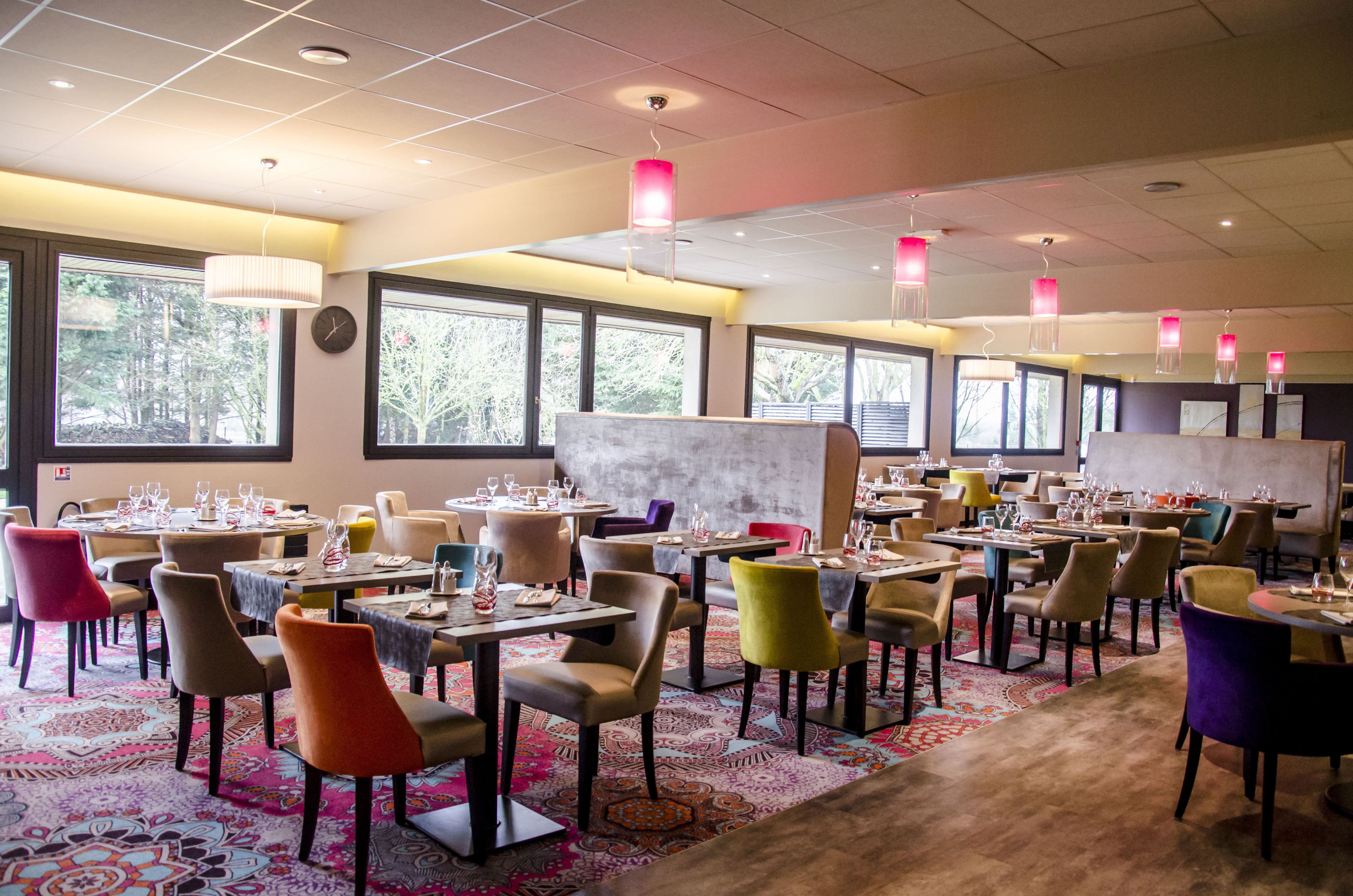 A restaurant with multiple tables and chairs, large windows, and hanging pendant lights.