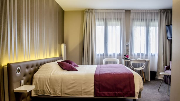 Une chambre d’hôtel avec un grand lit, un bureau, une chaise et un téléviseur.
