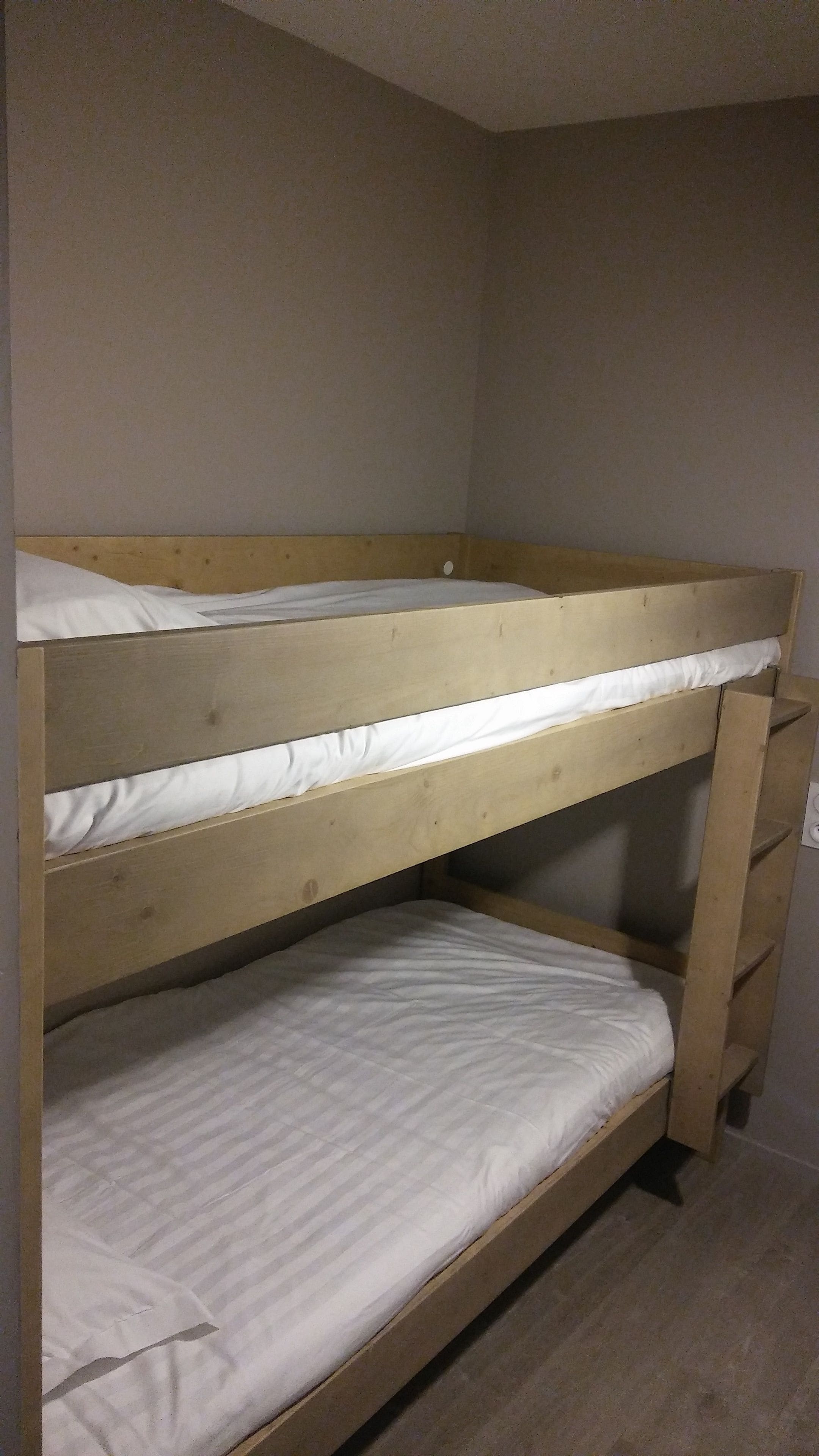 Una cama litera con dos niveles, cada uno con un colchón blanco.
