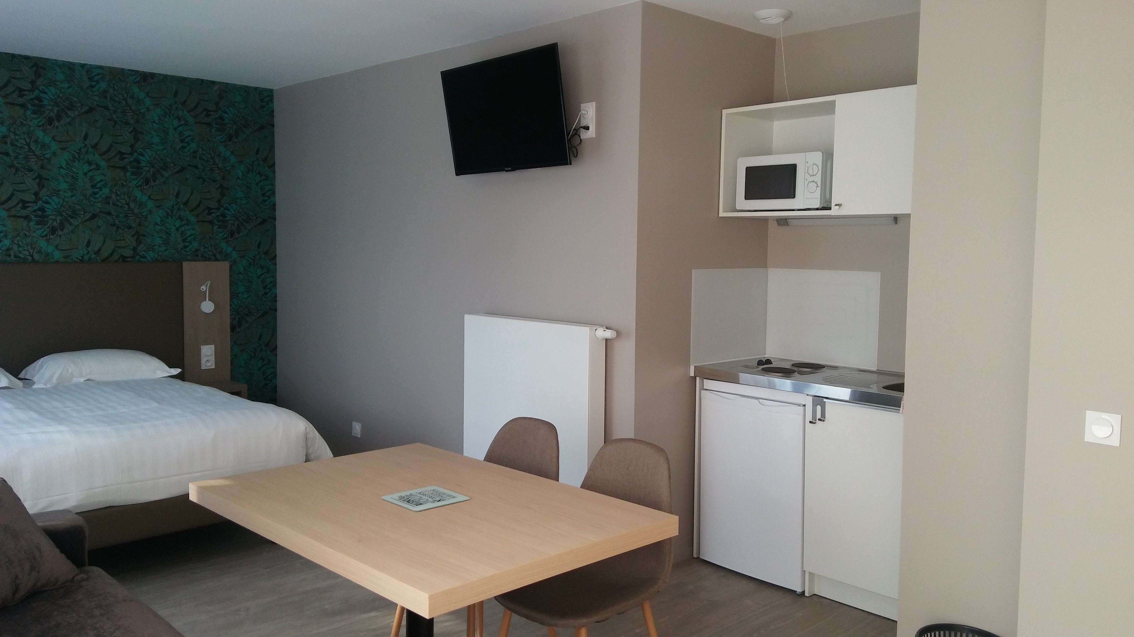 Quarto de hotel compacto com cama, uma pequena mesa, micro-ondas e cozinha compacta.