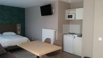 Quarto de hotel compacto com cama, uma pequena mesa, micro-ondas e cozinha compacta.
