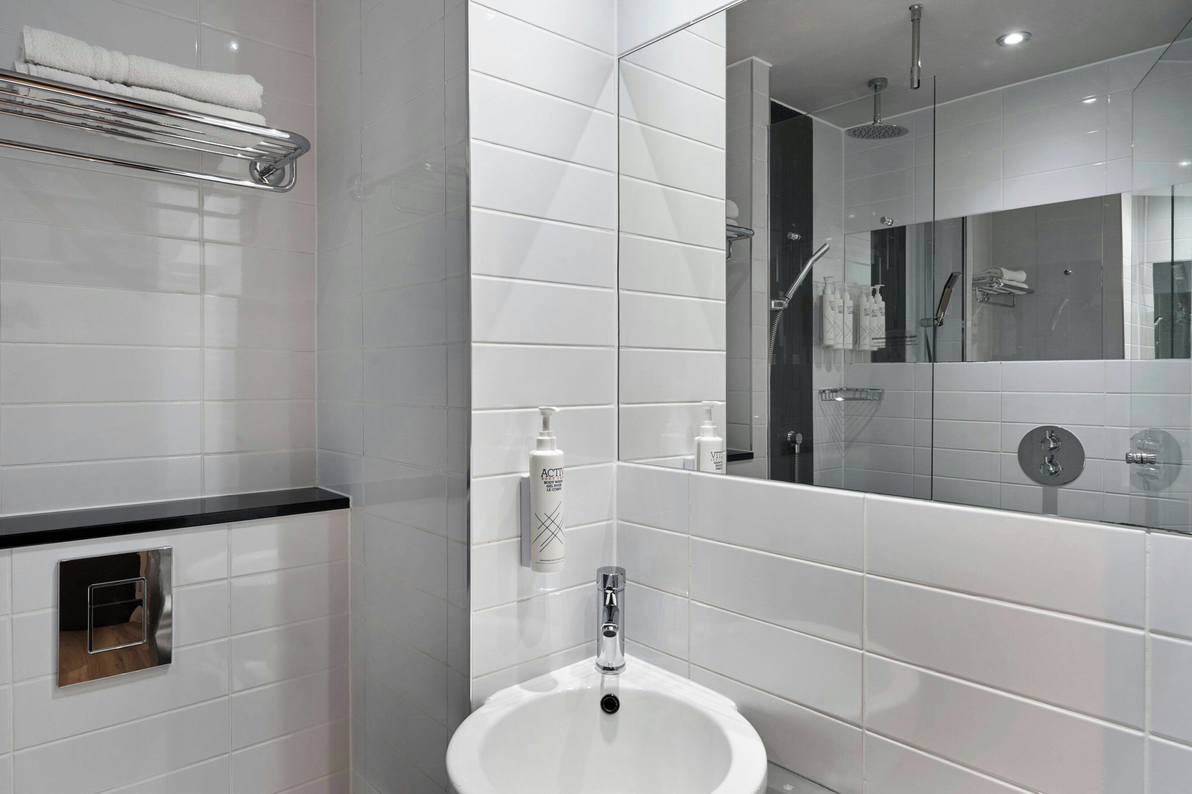A modern bathroom with white tiles, a sink, a mirror, and a shower area.