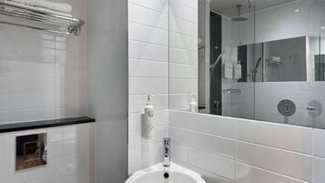 Un baño moderno con azulejos blancos, un lavabo, un espejo y una zona de ducha.