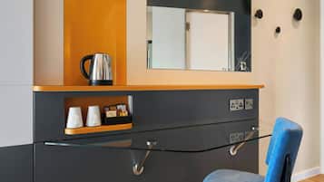 A modern room with a glass partition, a blue chair, a coffee maker, and a shelf with cups and a clock.
