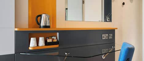 A modern room with a glass partition, a blue chair, a coffee maker, and a shelf with cups and a clock.