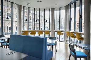 Un comedor moderno con asientos azules y sillas amarillas, amplias ventanas que ofrecen vistas de arquitectura histórica.