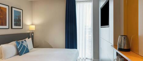A hotel room with a bed, a TV, a coffee maker, and a window with curtains.