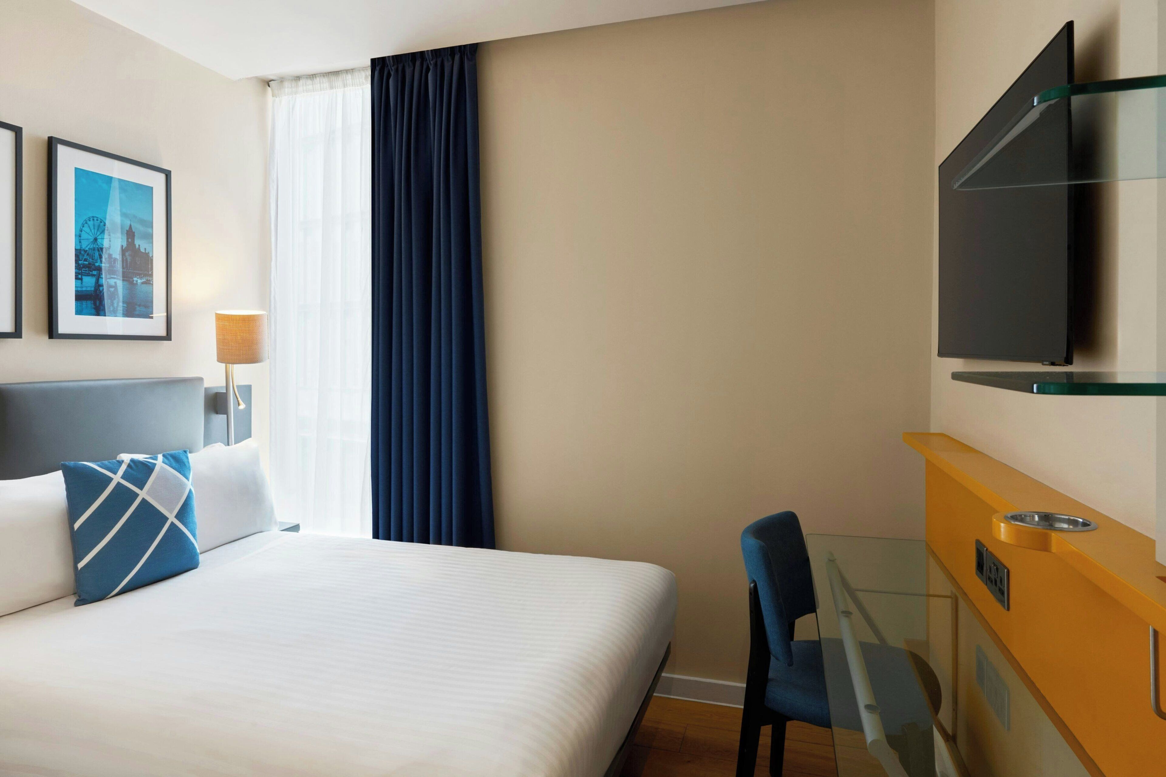 A hotel room with a bed, a desk, a chair, a television, and a window with curtains.
