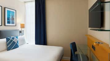 A hotel room with a bed, a desk, a chair, a television, and a window with curtains.