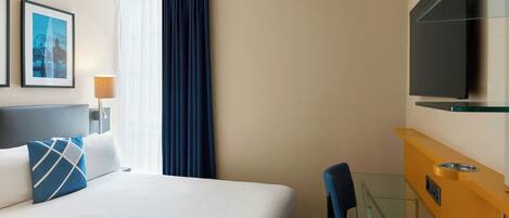A hotel room with a bed, a desk, a chair, a television, and a window with curtains.