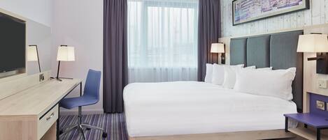 A hotel room with a bed, desk, chair, and a large window with curtains.