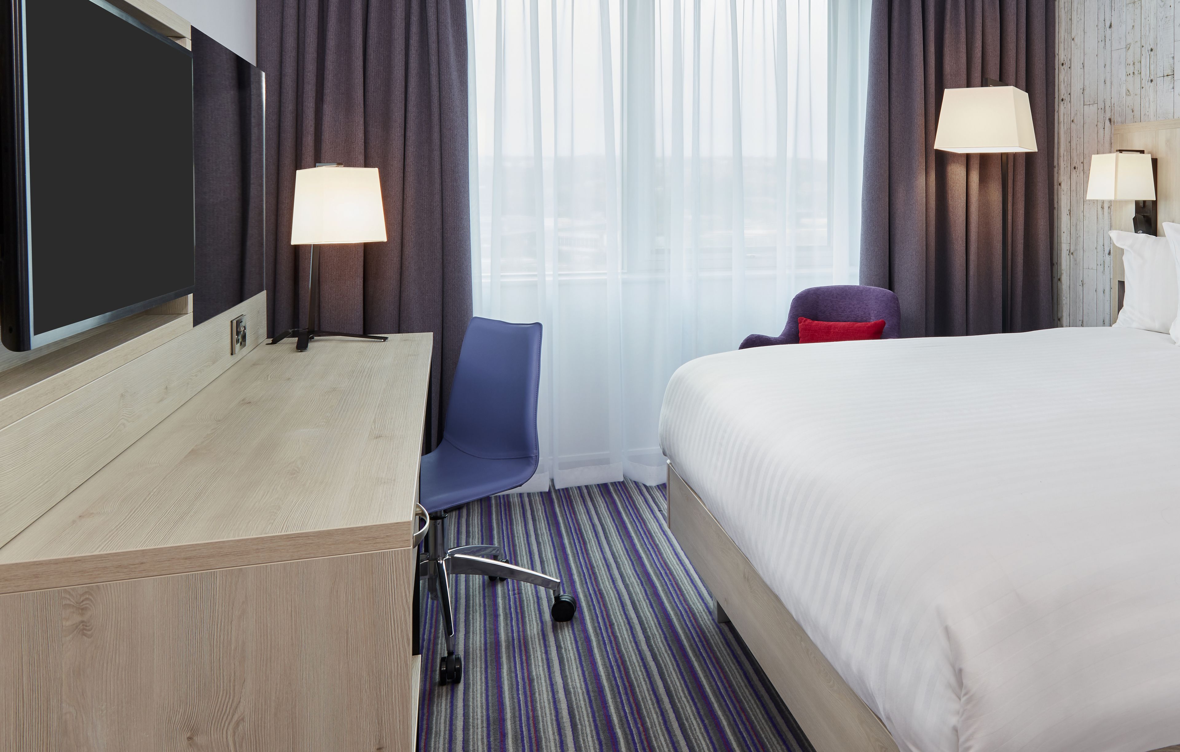 A hotel room with a bed, desk, chair, and two lamps.