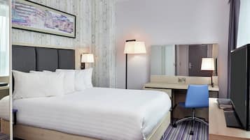 A hotel room with a bed, desk, chair, and a large mirror.