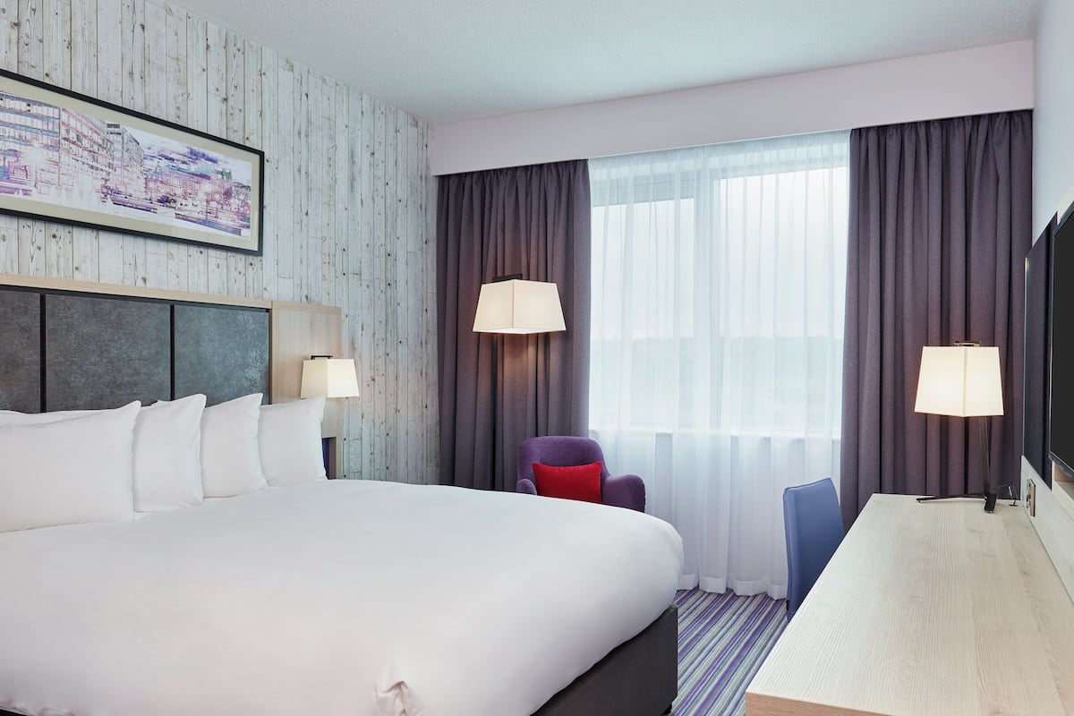 Habitación de hotel con una cama grande, dos lámparas de noche, un escritorio con una silla y una ventana con cortinas.