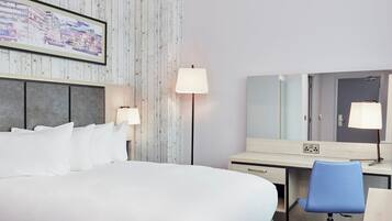 A hotel room with a bed, bedside lamps, a desk with a chair, a large mirror, and a wall-mounted TV.