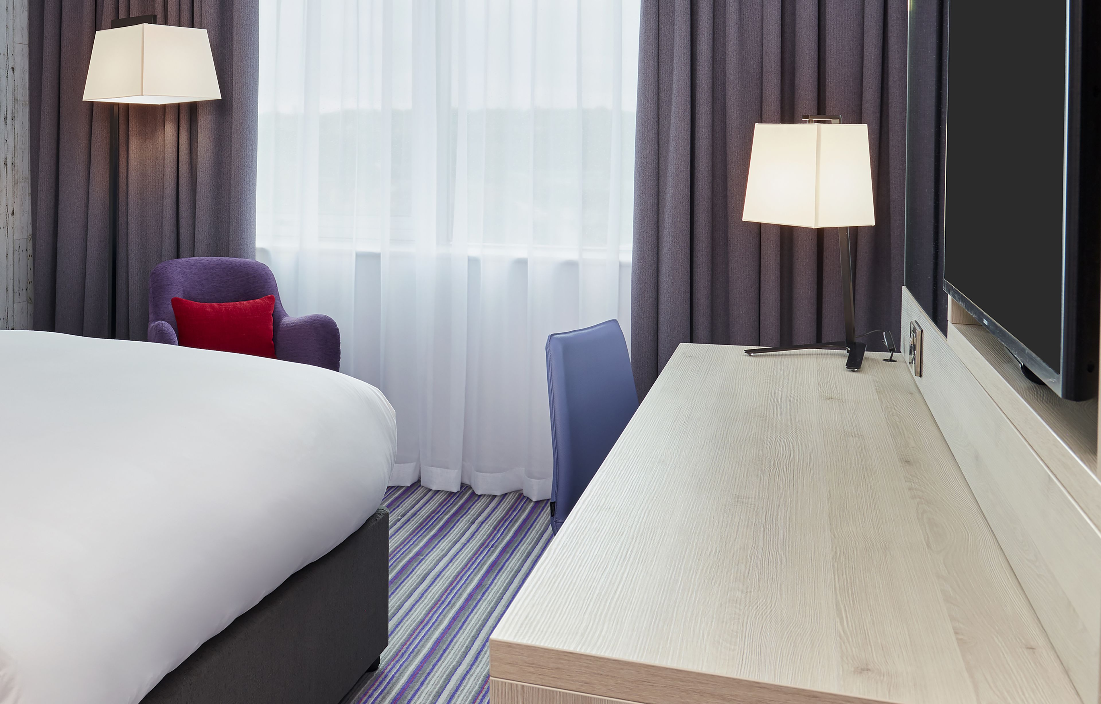 Ett hotellrum med en säng, två stolar, ett skrivbord och två lampor.