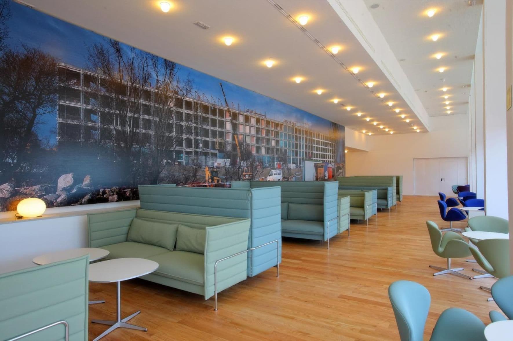 Un interior moderno con asientos verdes, un mural y suelo de madera.