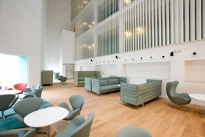 A modern interior with seating areas, a high ceiling, and a large window. - Hotel Hiberus (Zaragoza)