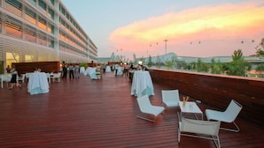 A rooftop dining area with tables and chairs, overlooking a cityscape during sunset. - Hotel Hiberus (Zaragoza)