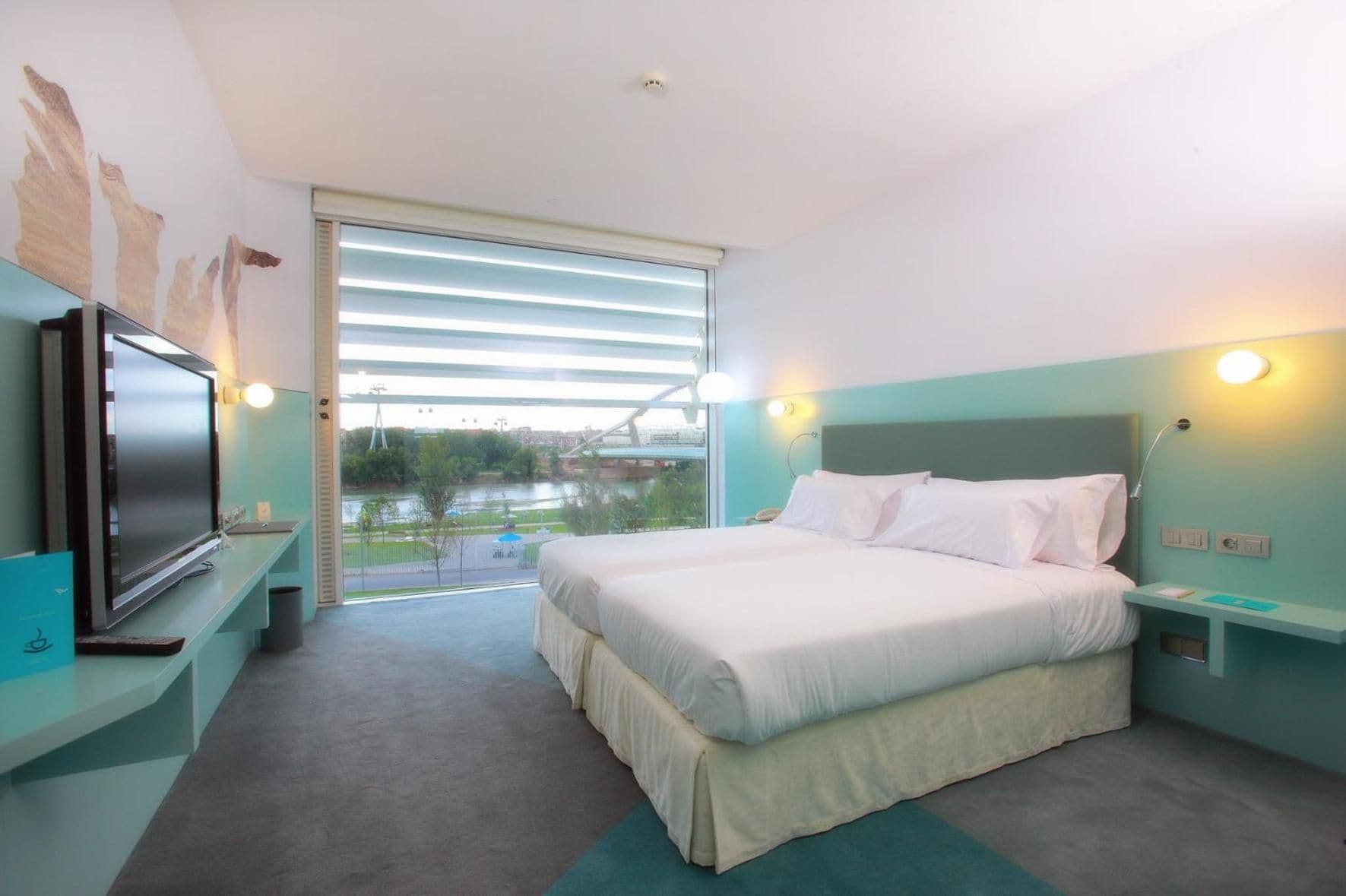 Habitación de hotel moderna con una cama grande, televisión y vistas a un puente y un río.