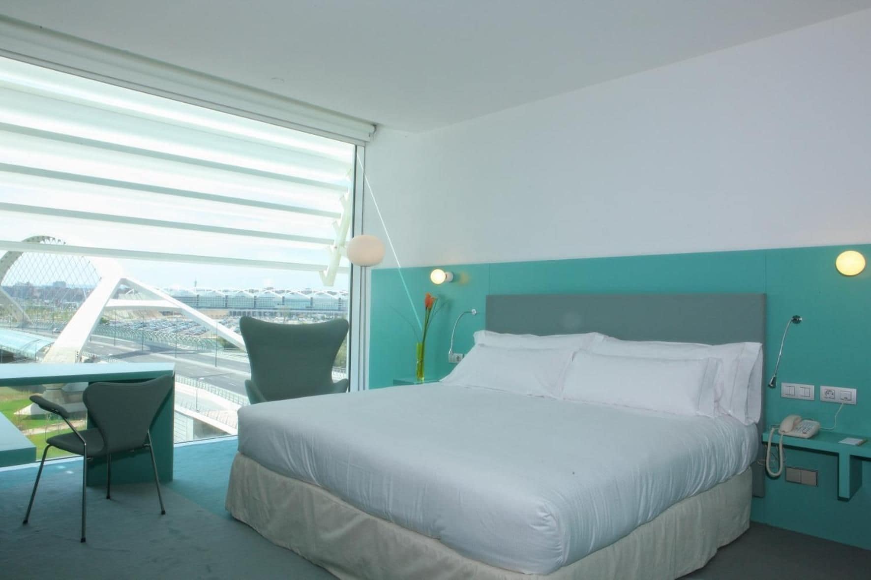Una camera d'albergo moderna con un letto grande, una scrivania e vista su un ponte e sullo skyline della città.