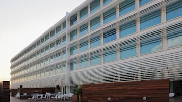 Un edificio moderno con varios pisos, grandes ventanales y un área de estar al aire libre con mesas y sillas.
