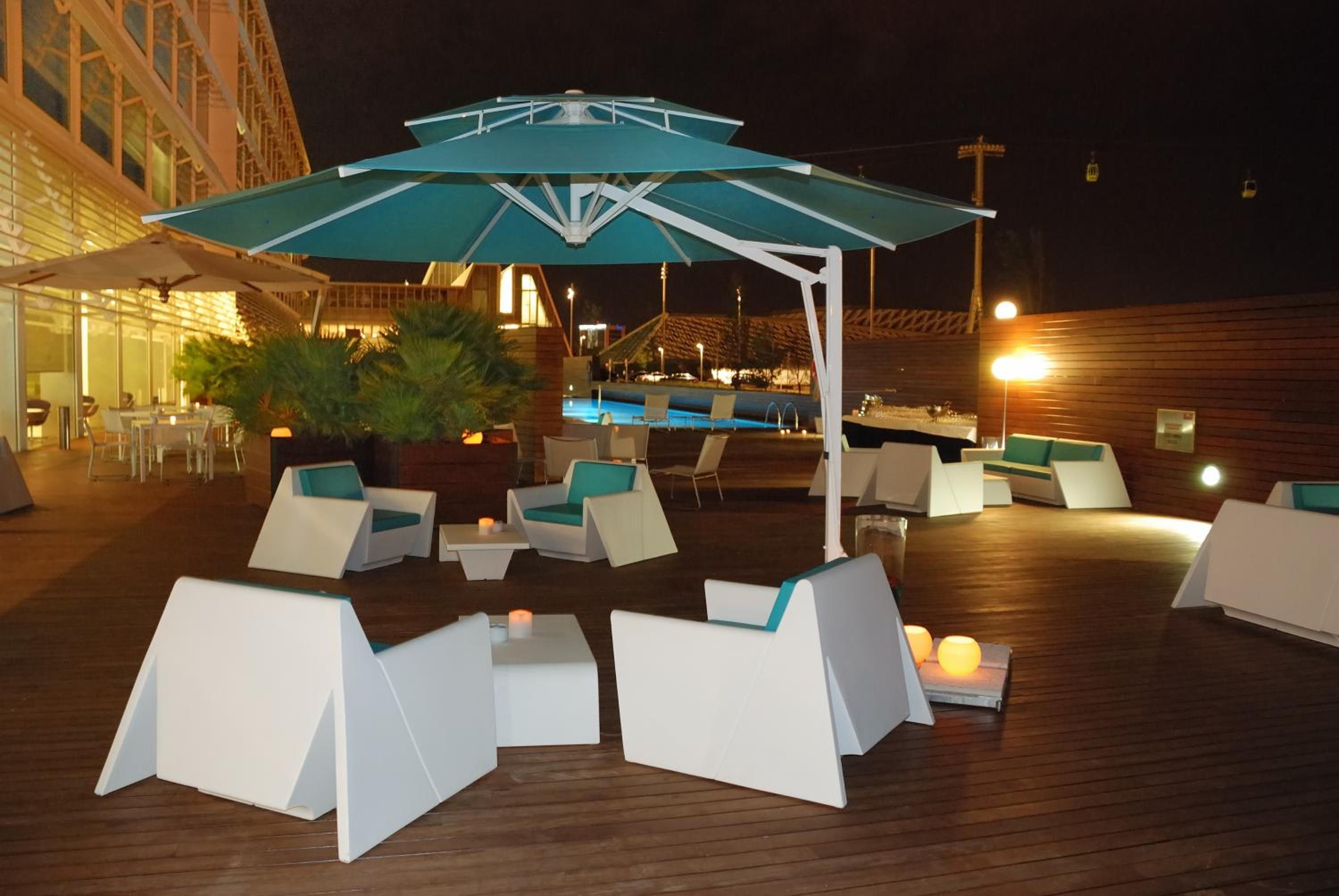 An outdoor seating area with white tables and chairs, a pool, and a covered umbrella.