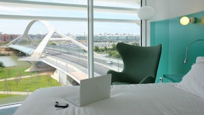 A hotel room with a bed, a laptop, and a view of a bridge and road. - Hotel Hiberus (Zaragoza)