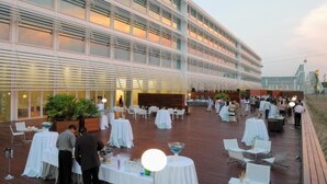 An outdoor event space with multiple tables and chairs, a large building in the background, and a clear sky. - Hotel Hiberus (Zaragoza)