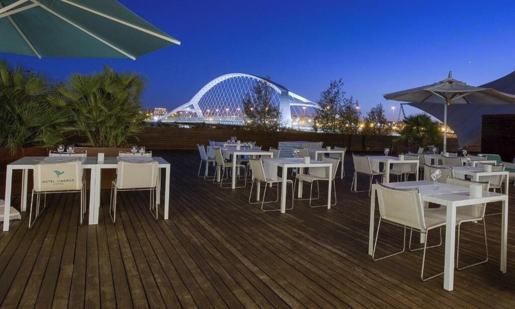 Een buitenterras met tafels en stoelen, een houten dek en een grote parasol.