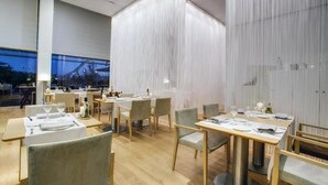 Un restaurant moderne avec des tables et des chaises en bois, une grande fenêtre et un mur à texture.