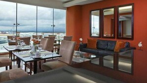 A dining area with tables and chairs, a sofa with cushions, and large windows offering a view. - Sand Diamond Hotel (Colon)