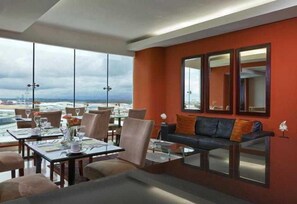 Un espace repas avec des tables et des chaises, un canapé avec des coussins et de grandes fenêtres donnant sur un paysage.