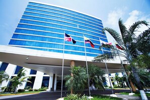 A modern hotel with a curved facade, multiple flags, and palm trees. - Sand Diamond Hotel (Colon)
