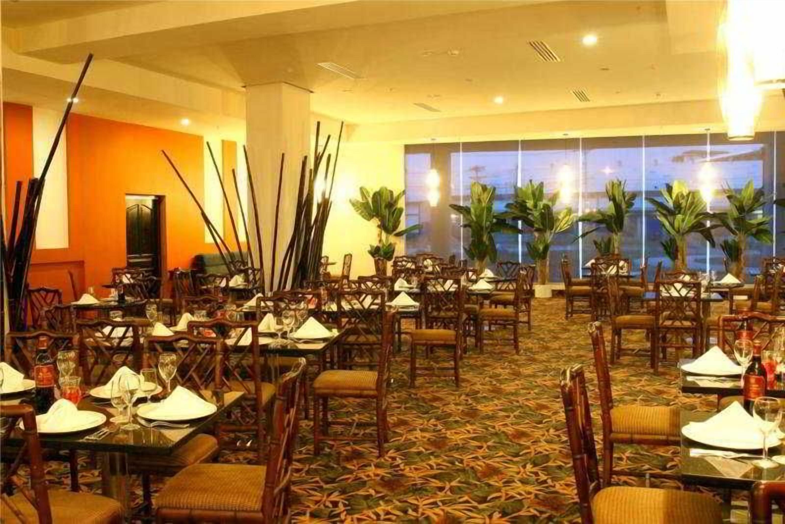 Un restaurant doté de nombreuses tables et chaises, d’un tapis à motifs et de grandes fenêtres offrant une belle vue.
