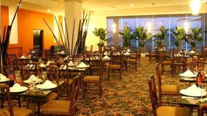 A restaurant with multiple tables and chairs, a patterned carpet, and large windows with a view. - Sand Diamond Hotel (Colon)