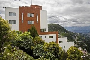 Un bâtiment moderne à deux étages, doté d’un toit plat et d’une façade en briques, entouré d’une végétation luxuriante et offrant une vue sur un paysage vallonné.