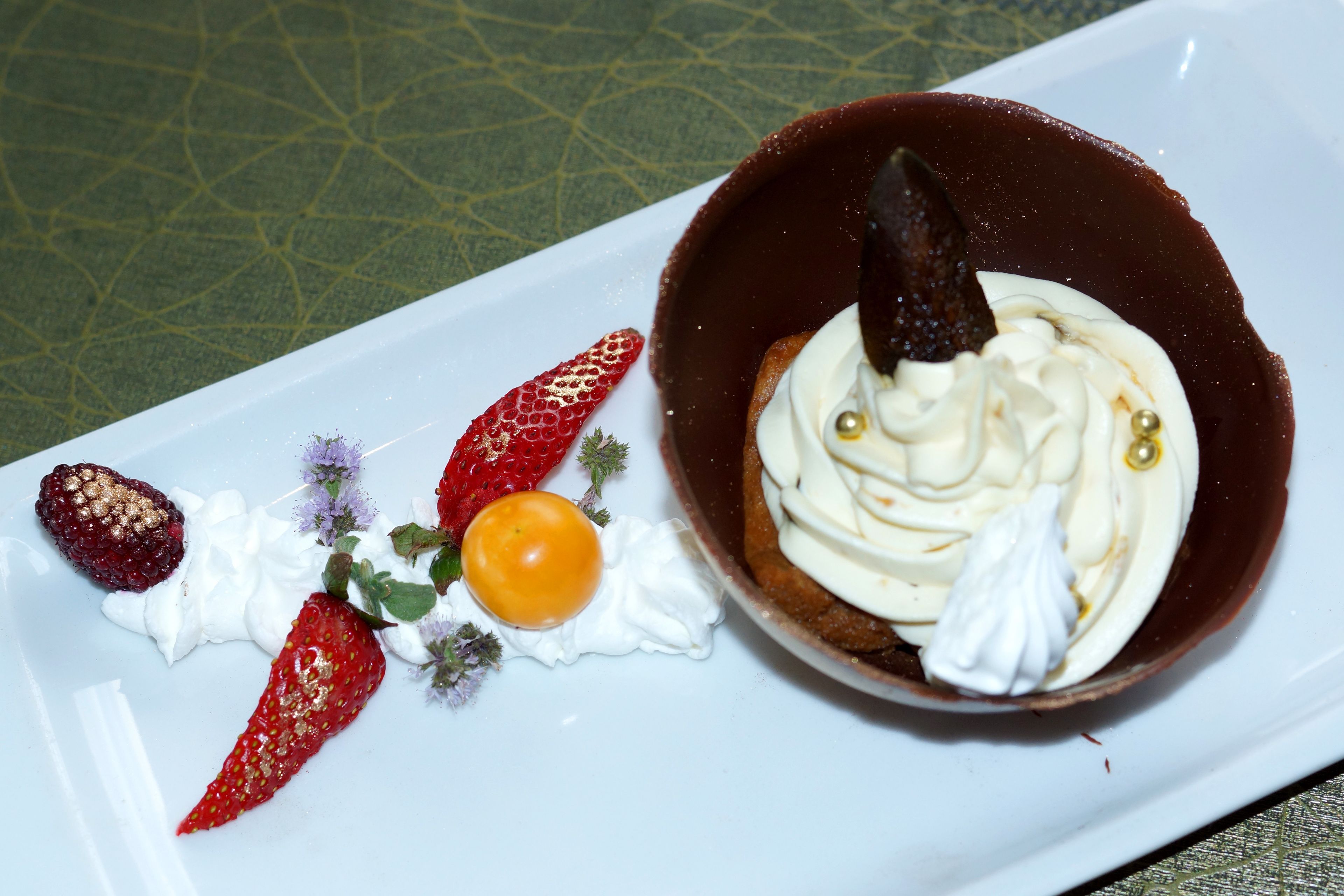 Une assiette à dessert avec une coupe en chocolat, des fraises et une cerise.