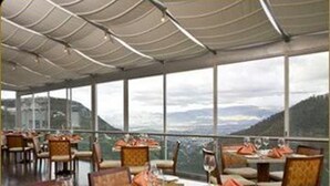 Ein Restaurant mit gedeckten Tischen, großen Fenstern mit Bergblick und einem modernen Deckenstil.