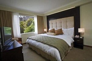 Une chambre d’hôtel avec un grand lit, deux tables de chevet avec des lampes, un téléviseur posé sur un bureau et une fenêtre avec des rideaux.