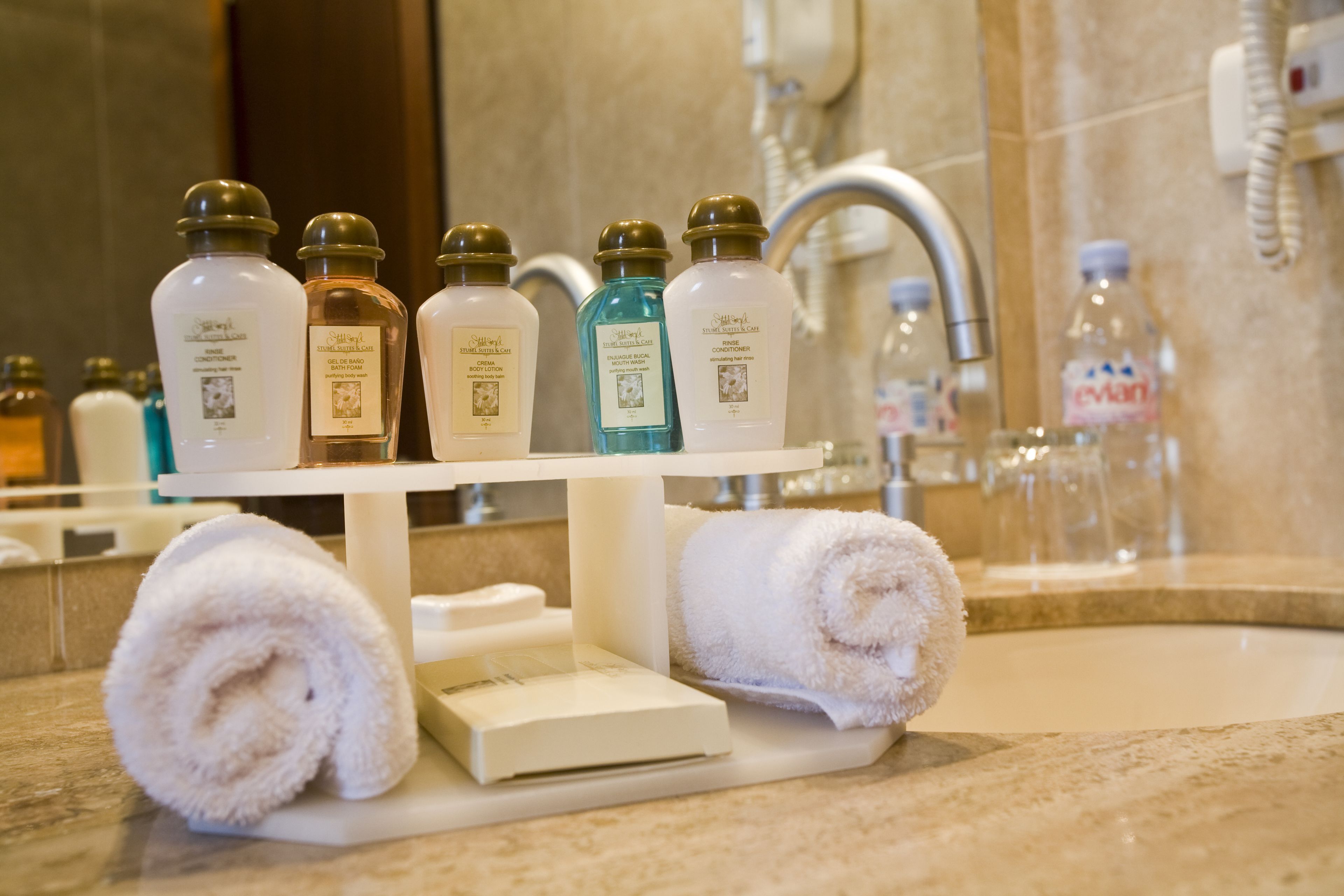 Une salle de bain avec un lavabo, plusieurs flacons de produits de toilette et deux serviettes enroulées sur un plateau.