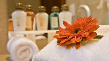 A bathroom with a towel, a flower, and toiletries on a shelf.