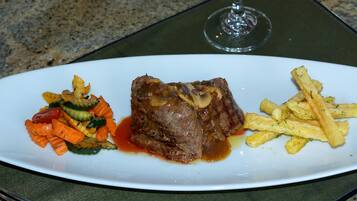Un plato con carne, verduras y papas fritas sobre una mesa, junto a una copa de vino.