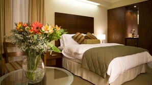 Ein Hotelzimmer mit einem Bett, einem Nachttisch, einem Beistelltisch mit Blumenvase, einem Sessel und einem Kleiderschrank.