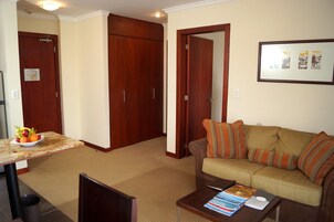 Una sala de estar con un sofá marrón, una mesa de centro con libros y una computadora portátil, un comedor con una mesa y sillas, y un cuadro en la pared.